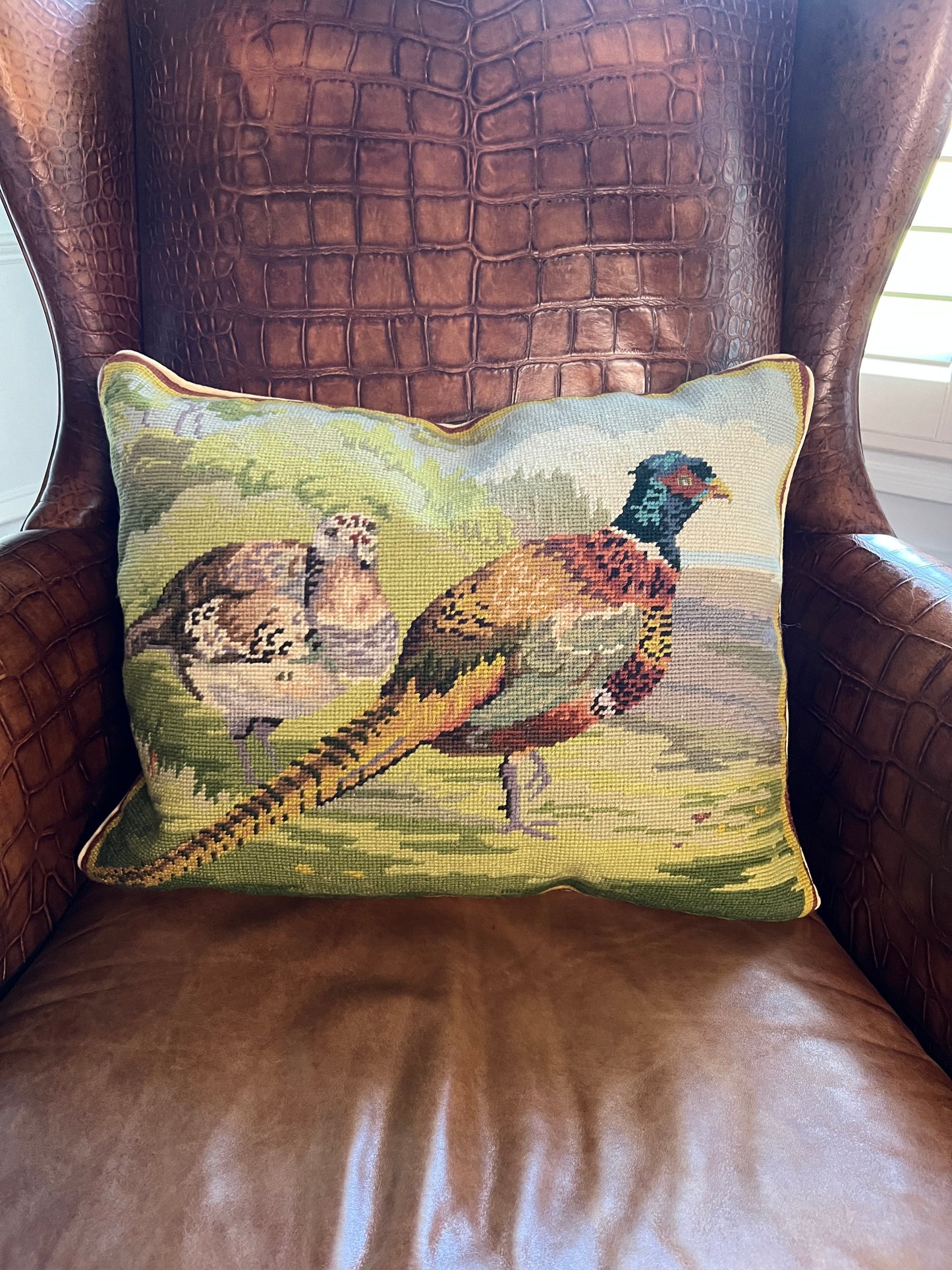 16x20 needlepoint pillow with pheasant and grouse on a brown leather wingback chair.