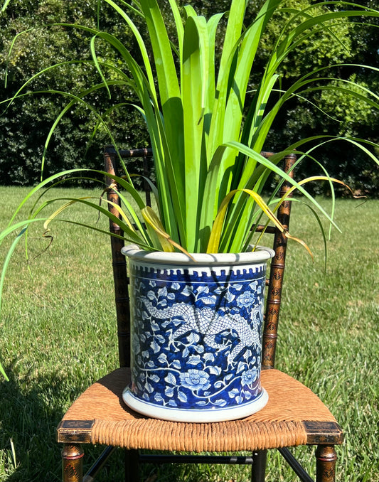 Cobalt blue porcelain cachepot with raised dragon and floral design, displayed outdoors on a woven seat with tall green plant.