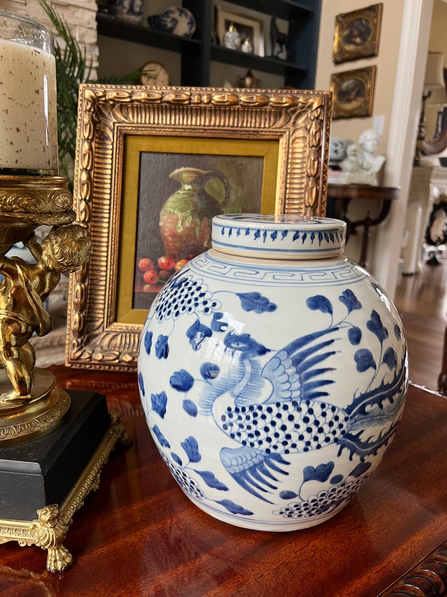 Hand-painted blue and white phoenix porcelain jar on a wood table beside a gold frame and decor.