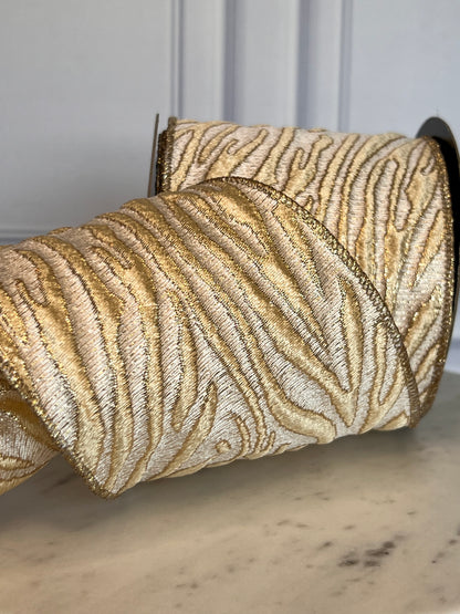 A close-up of a roll of textured ribbon with a metallic gold and champagne zebra-stripe pattern, resting on a light marble surface.