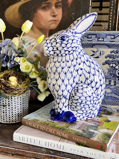 Decorative blue and white ceramic rabbit on a surface with books and flowers.