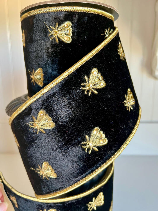 Black velvet ribbon with gold embroidered bee motifs displayed on a spool.