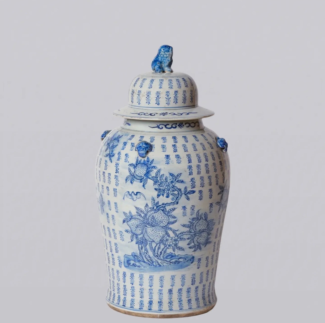 Large blue and white porcelain longevity temple jar featuring peaches, flowering branches, traditional motifs, and a foo lion finial lid.