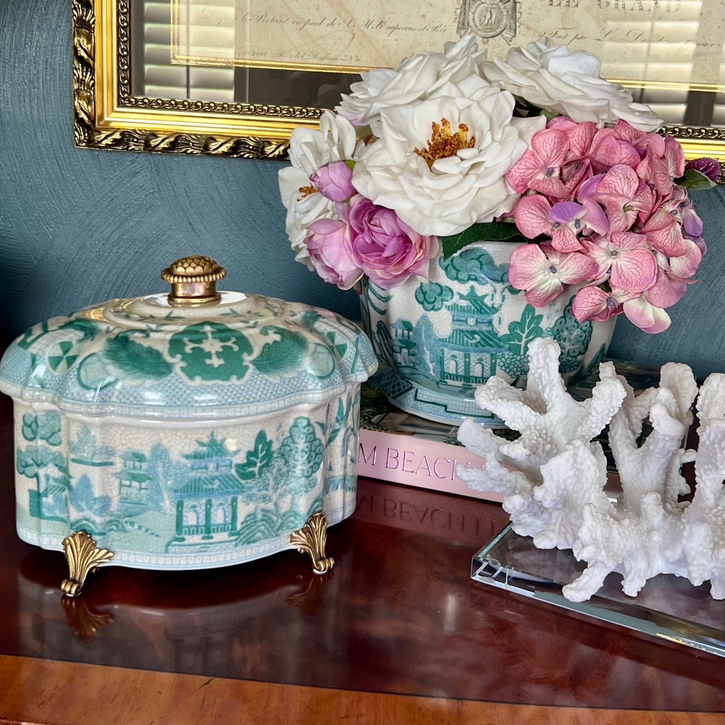 Turquoise chinoiserie porcelain lidded box with pagoda and garden motifs, styled on a wood table with flowers and coral decor.
