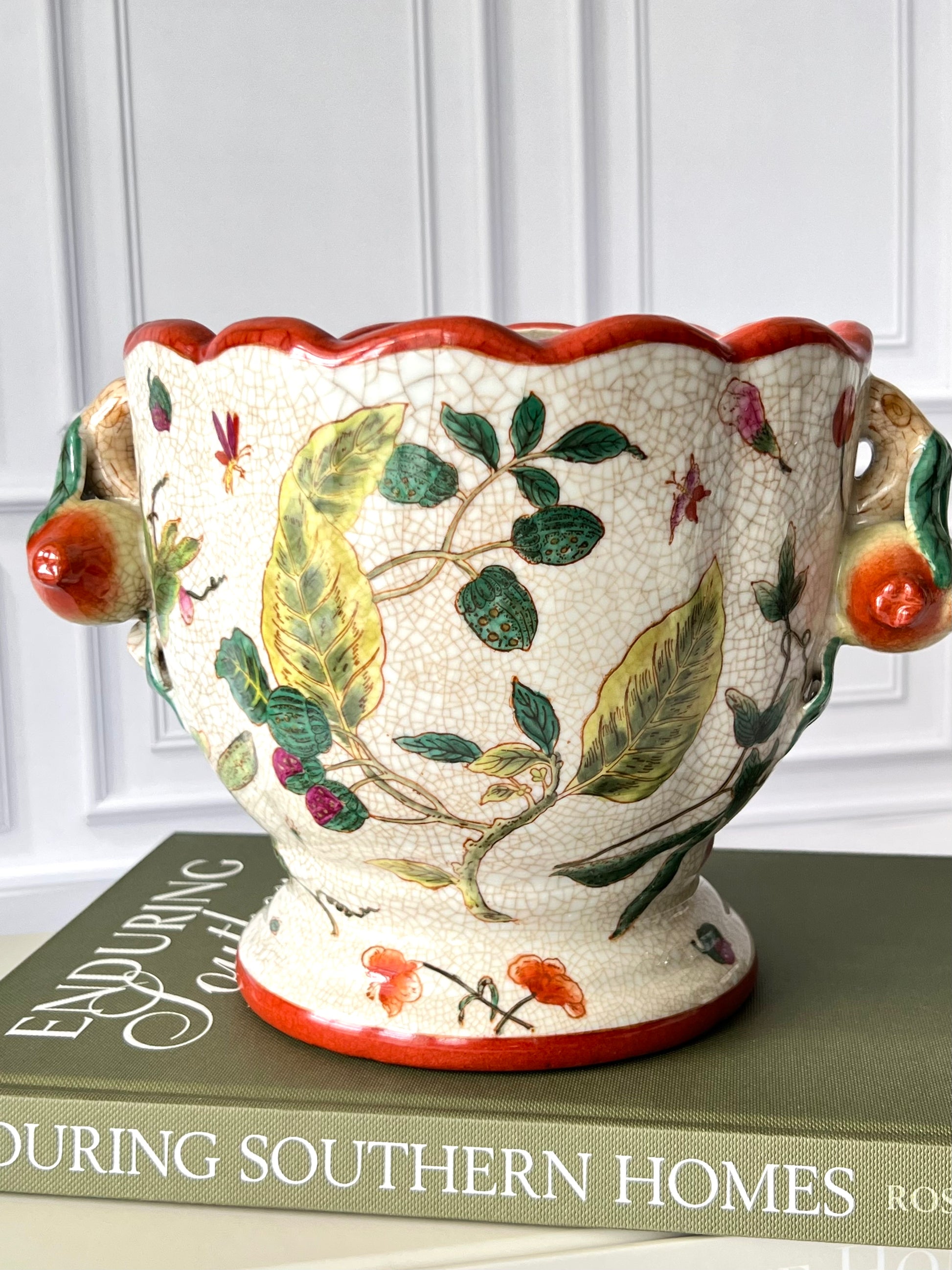 Chinoiserie planter with antiqued crackle finish, scalloped rim, and leaf and berry motif, styled on a green book with figural fruit handles