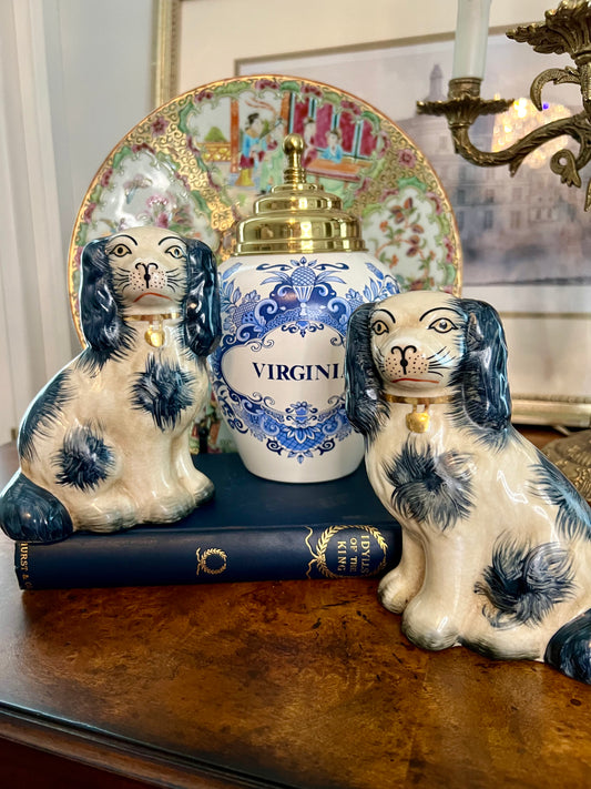 Blue and cream Staffordshire-style spaniel dog figurines displayed with a blue-and-white Virginia tobacco jar and a famille rose plate in an elegant vignette.